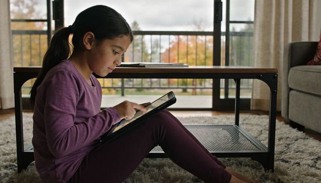 Young girl using tablet while sitting on shag rug in living room with autumn view