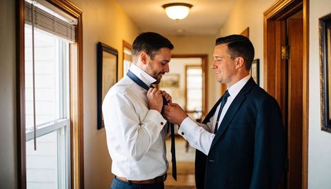 Groom getting help with necktie from best man in home hallway morning wedding prep