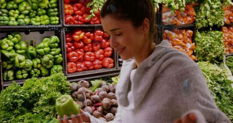 Woman inspecting green bell peppers in grocery store