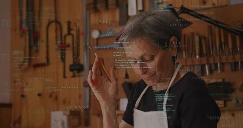 Senior craftswoman inspecting woodwork, jotting notes in workshop with code overlay