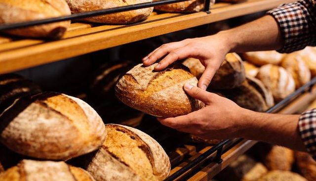 Hands selecting rustic sourdough loaf on wooden bakery shelves, artisanal bread display