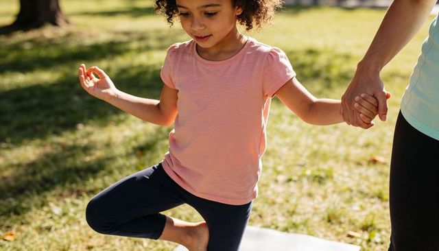Child practicing tree pose in park holding guardian hand sunlit outdoor family wellness