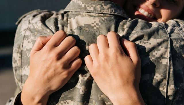 Military homecoming embrace partner hugging soldier in digital camouflage uniform
