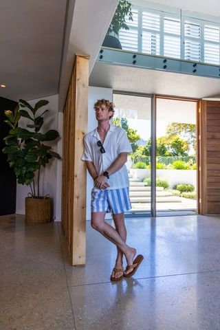 Man leaning in modern coastal foyer wearing striped shorts and sandals by glass doors