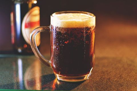 Frothy Dark Beer Mug with Condensation on Bar Counter under Warm Amber Lighting