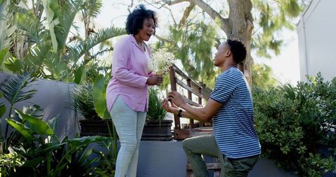 Man proposing to woman outdoors amidst lush greenery