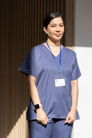 Confident female nurse standing in clinic corridor wearing navy scrubs and badge