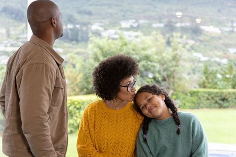 Diverse family sharing tender moment mother kissing daughter on terrace with hillside view