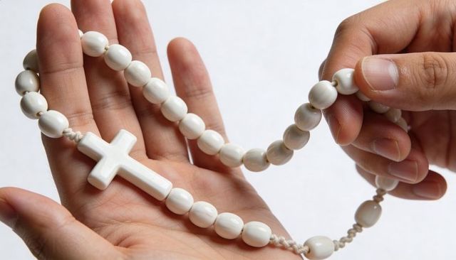 Holding white rosary beads with glossy crucifix, close-up of hands and palms