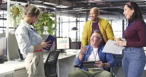 Inclusive office team collaborating around colleague in wheelchair in bright open workspace