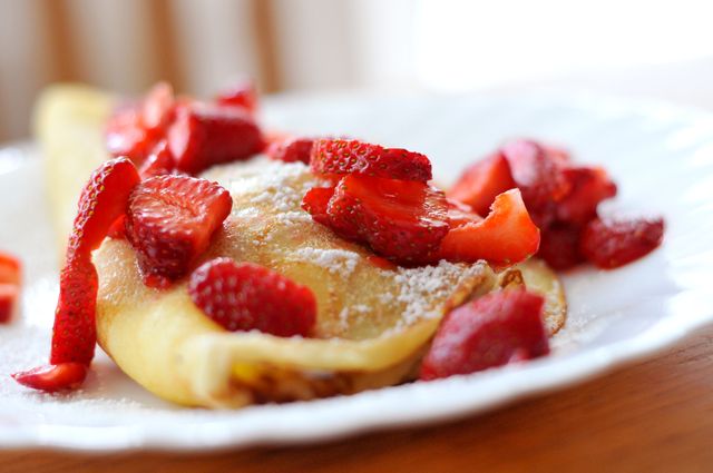 Close-up of a strawberry crepe topped with fresh strawberries and powdered sugar. Suitable for use in food blogs, restaurant menus, breakfast promotions, or any content related to delicious desserts or sweet breakfast options.