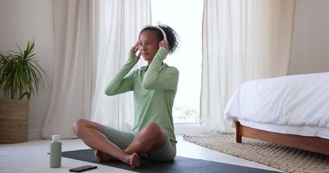 Woman in Sportswear Meditating with Headphones in Bedroom