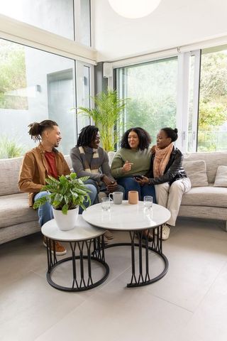 Diverse friends chatting on modern living room sofa with smartphone and indoor plants