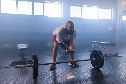 African american man chalking hands before deadlift, preparing for heavy lift in hazy gym