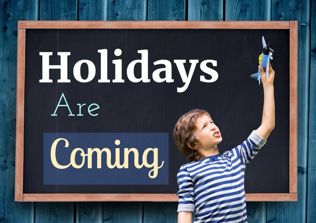 Young boy holding toy airplane in front of chalkboard sign announcing holidays. Ideal for use in holiday promotions, festive announcements, and childhood-themed content.