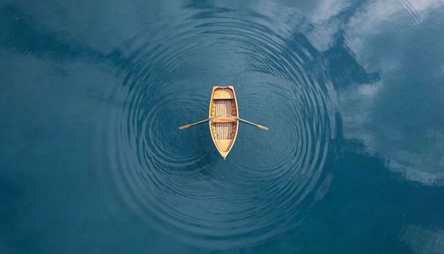 Aerial wooden rowboat floating on blue water creating circular ripples and reflection