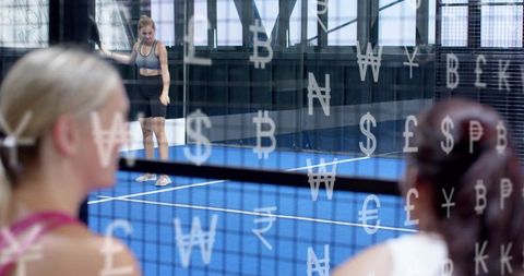 Female athlete standing on blue court behind currency-symbol glass while spectators watch