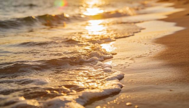 Golden sunset waves lapping shoreline with shimmering wet sand and white foam