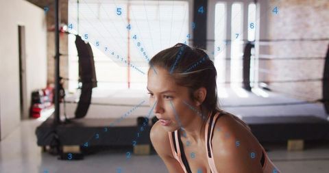 Female athlete catching breath after round in industrial boxing gym with data overlay