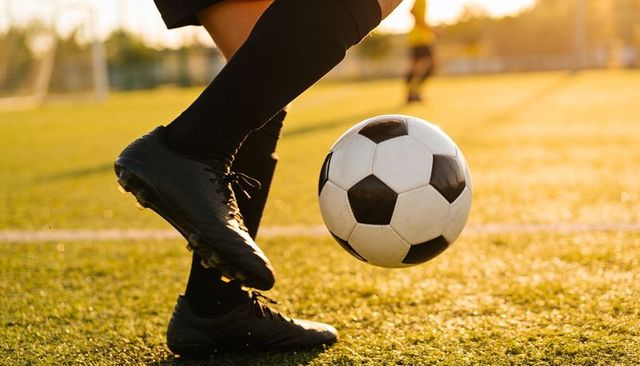 Sunlit soccer player controlling ball black cleats knee-high socks on artificial turf