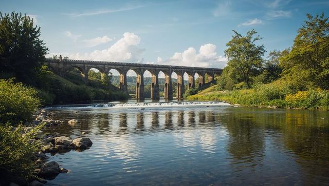 Stone railway viaduct spanning tranquil river with arched reflections and weir