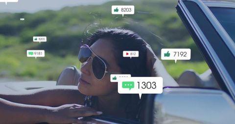 The image beautifully captures the essence of modern digital connectivity while experiencing freedom on the open road. A woman wearing aviator sunglasses leans against the window of a sleek convertible, symbols of digital engagement like likes and comments floating around her, representing online interaction. The background shows lush green hills under a clear blue sky. Perfect for use in stories or advertisements focused on digital marketing, social media engagement, adventure travel, or modern lifestyle themes.