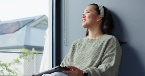 Relaxed Woman Sitting by Window with Tablet in Hand