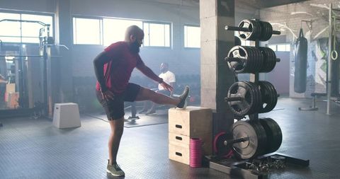 African men stretching and resting in sunlit industrial gym with plyo box and weights