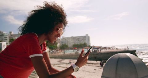 Young woman texting by sunny beach promenade