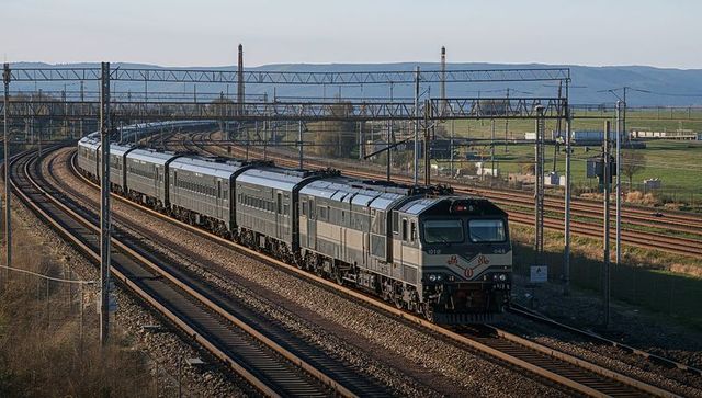 Rounding diesel-electric passenger train on curving rural tracks under overhead catenary