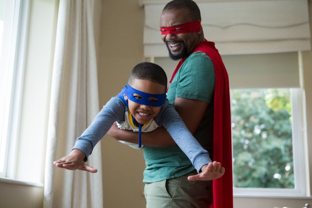 Father and son enjoying quality time together, dressed as superheroes with masks and capes. Perfect for themes related to family bonding, childhood imagination, playful parenting, and indoor activities. Ideal for use in parenting blogs, family-oriented advertisements, and educational materials promoting family engagement.