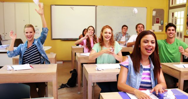 High school students expressing excitement and joy in a classroom setting while throwing paper. Ideal for use in educational materials, school brochures, student engagement articles, and youth-related promotional content.
