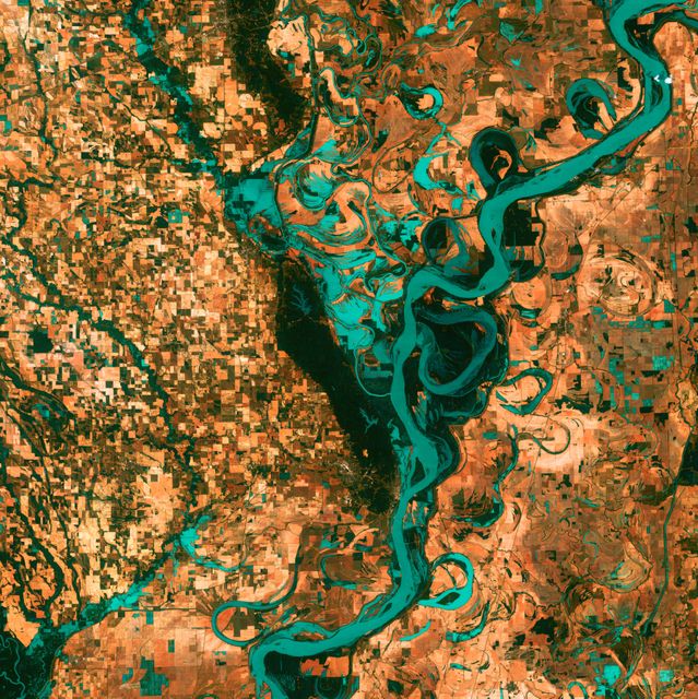 This image vividly captures the winding curves of the Mississippi River as seen from above. Towns, fields, and pastures are clearly visible surrounding the river, showing a beautiful contrast in natural and human-made elements. Ideal for educational materials, environmental studies, geographical documentation, and public presentations highlighting river geomorphology and land use patterns.