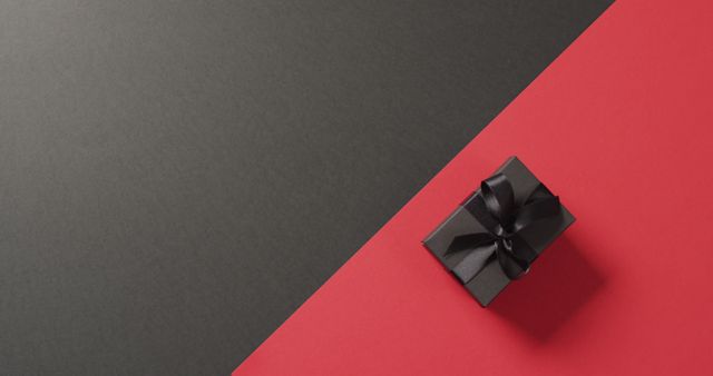 Depicts an elegant black gift box with ribbon on a contrasting black and red background. Great for use in holiday promotions, gift websites, advertising luxury products, minimalist design projects, and greeting cards.