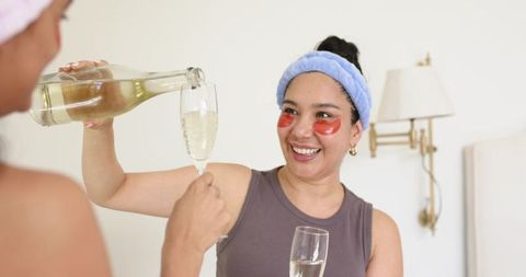 Diverse friends enjoying spa night pouring champagne wearing under-eye gel patches