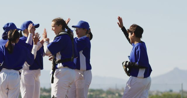 Group of baseball players in blue uniforms celebrating their victory with high fives on a sunny outdoor field. Ideal for sports-themed projects, teamwork promotional materials, and motivational posters or articles about sportsmanship and cooperation.