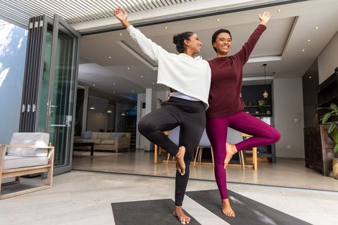 African american and indian women practicing tree pose together on home patio