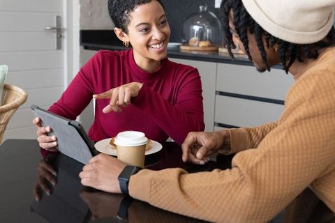 African american friends pointing at tablet over coffee and pastry, sharing ideas and smiling
