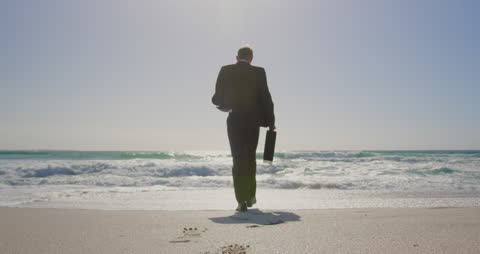 Businessman Walking Towards Ocean on Sunny Beach