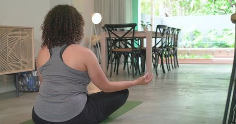 African american woman meditating on yoga mat in sunlit living room for wellness and calm