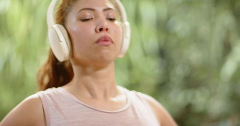 Young woman listening to guided meditation with wireless headphones outdoors for wellness