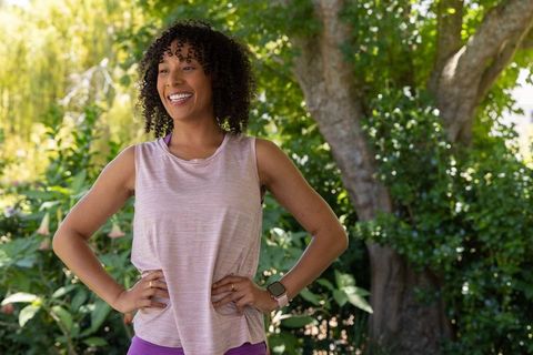 Smiling african woman wearing smartwatch and activewear posing in sunlit garden