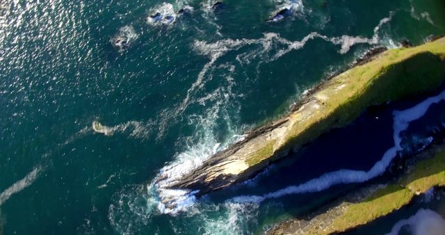 Aerial view captures the dynamic interaction between the ocean waves and a rugged coastline, with copy space. The contrasting textures and colors highlight the natural beauty and power of the coastal environment.