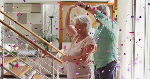 Elegant Senior Couple Dancing at Home Under Falling Confetti