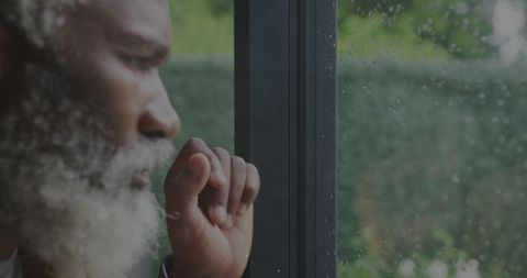 Elderly man contemplatively looking through rainy window