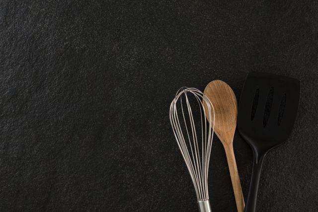 Whisker, wooden spoon and spatula on black background