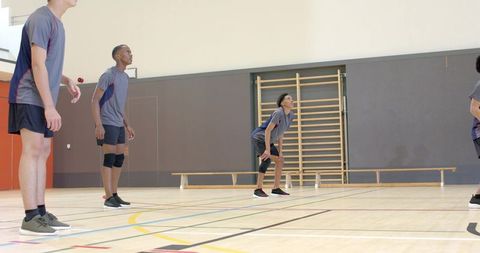 Teen volleyball team practicing defensive drill on indoor hardwood court