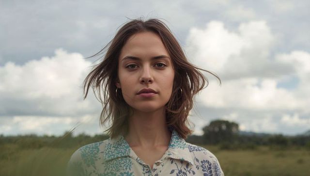 Windblown young woman portrait in meadow wearing floral blouse and hoop earrings