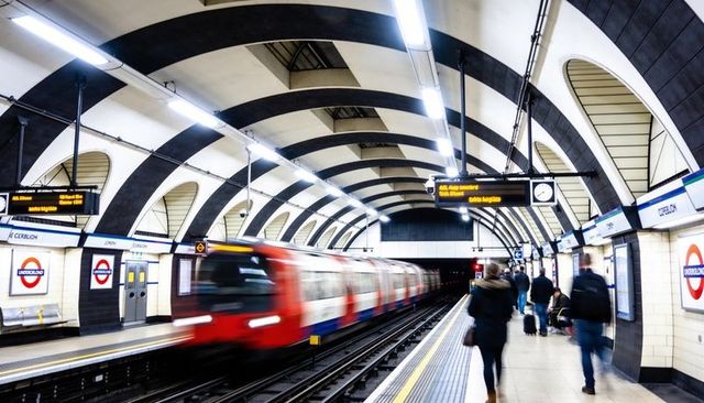 Speeding london underground train racing through arched station while commuters wait