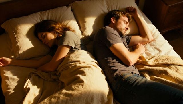 Couple sleeping back-to-back on bed in warm sunlit bedroom, cozy intimacy